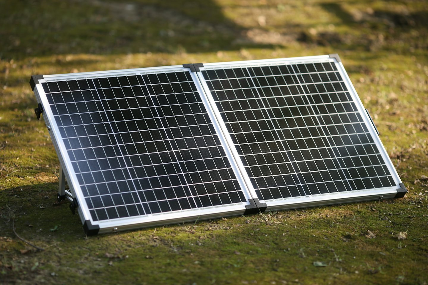A portable solar panel stands unfolded on green grass.