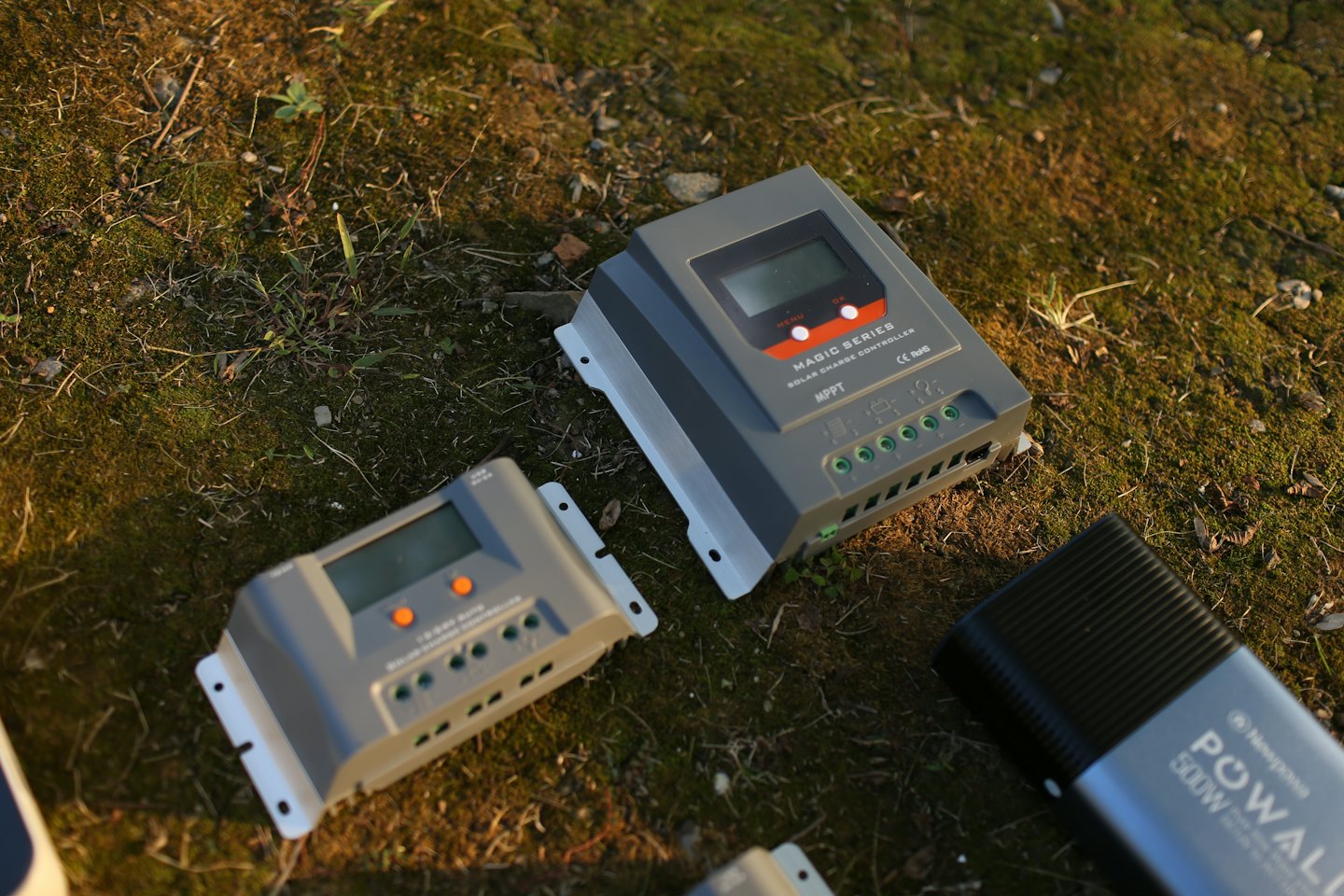 Solar charge controllers and a portable power station on mossy ground.